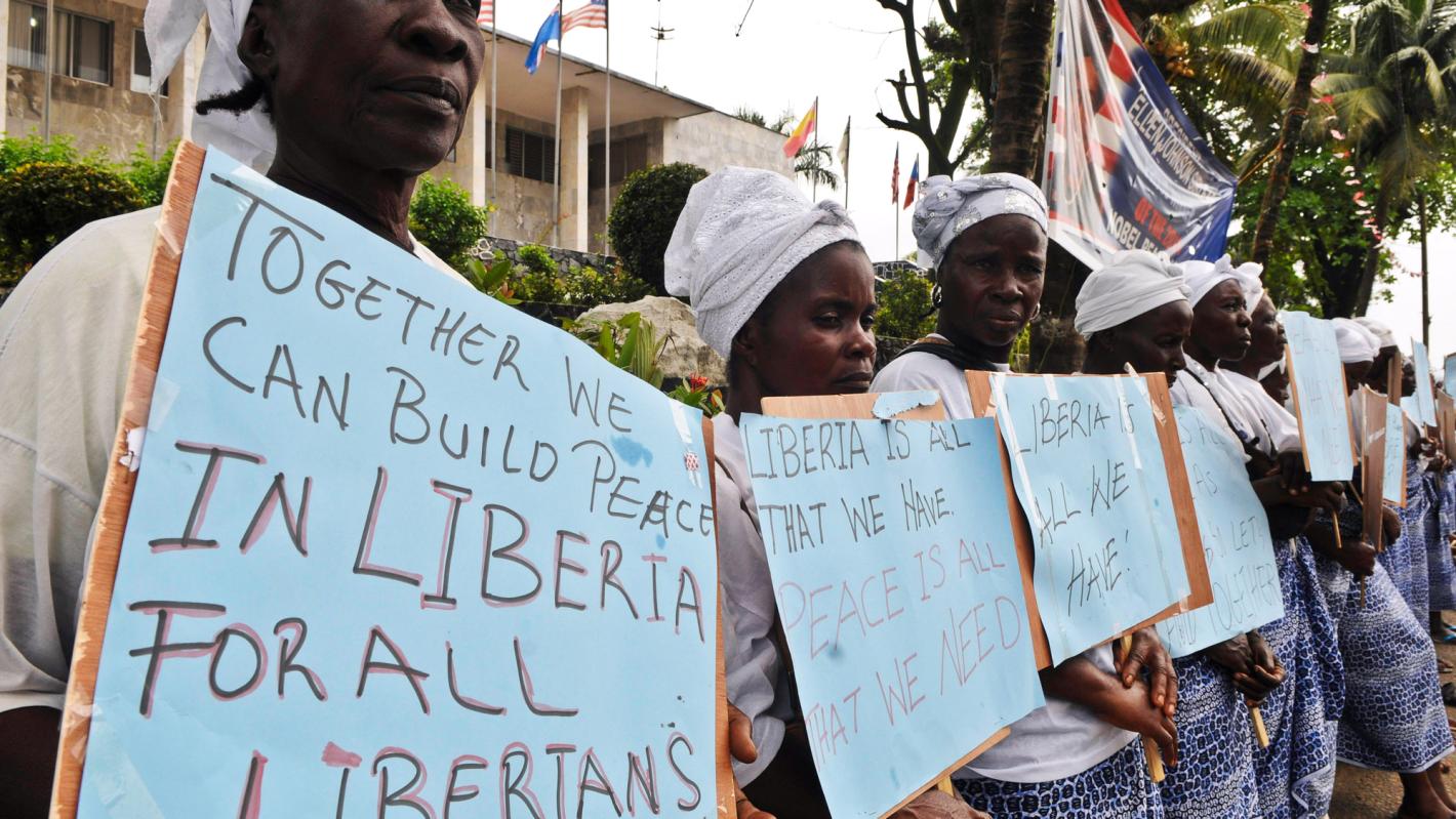 Women standing in a line holding hand written placards with messages for peace.