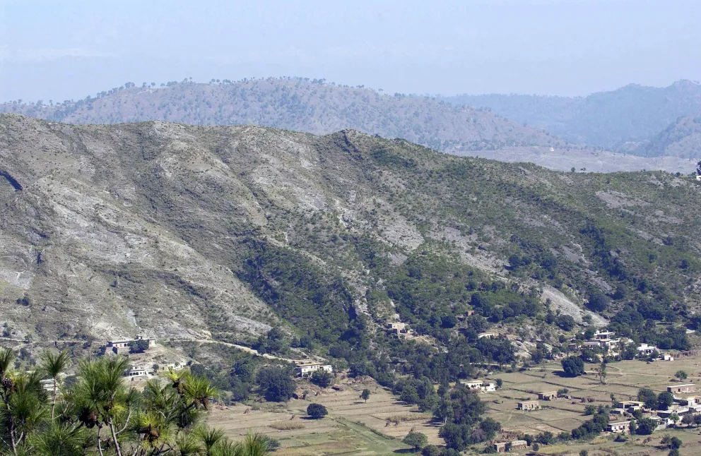 Mountainous terrain with scattered trees and small villages in valleys, under a clear blue sky.