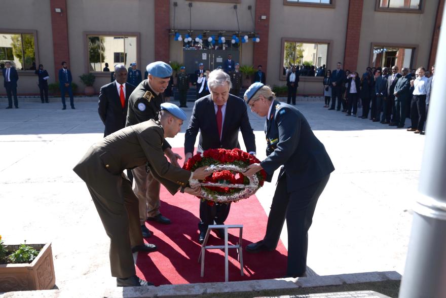 UN Secretary General Guterres lays a wreath during a formal ceremony, with uniformed personnel and others standing nearby.